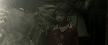 Movie still from “Vinyan” (2008), directed by Fabrice du Welz – A young boy wearing a red shirt and a pair of earrings; Close Up shot, High angle