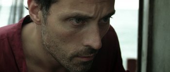 Movie still from “Vinyan” (2008), directed by Fabrice du Welz – A man's face in a dark room; Close Up shot, Low angle