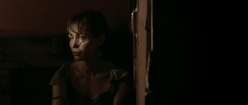 Movie still from “Vinyan” (2008), directed by Fabrice du Welz – A woman standing next to a door in a dark room; Close Up shot, Low angle