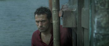 Movie still from “Vinyan” (2008), directed by Fabrice du Welz – A person standing near a body of water; Close Up shot, High angle