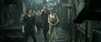 Movie still from “Vinyan” (2008), directed by Fabrice du Welz – A group of people walking across a bridge in the rain; Wide shot, Low angle
