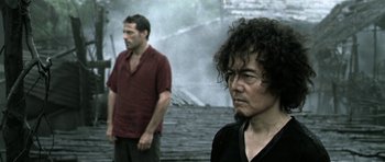 Movie still from “Vinyan” (2008), directed by Fabrice du Welz – Two men standing next to each other in front of a building; Close Up shot, Over the shoulder angle