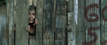 Movie still from “Vinyan” (2008), directed by Fabrice du Welz – An older woman leaning against a wooden fence; Medium shot, High angle
