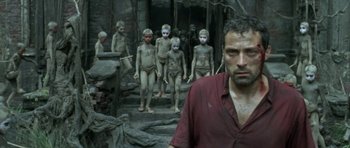 Movie still from “Vinyan” (2008), directed by Fabrice du Welz – A man standing in front of a group of people; Medium shot, Low angle