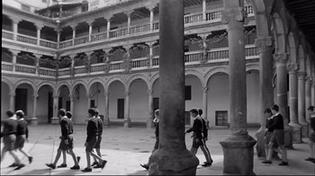 Movie still from “Viridiana” (1961), directed by Luis Buñuel – A black and white photo of a group of people walking in a courtyard; Wide shot, High angle
