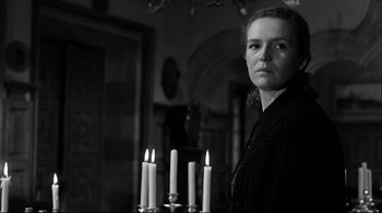 Movie still from “Viridiana” (1961), directed by Luis Buñuel – A woman standing in front of candles in a room; Medium shot, Low angle