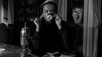 Movie still from “Viridiana” (1961), directed by Luis Buñuel – A woman sitting at a table drinking a cup of coffee; Medium shot, Low angle