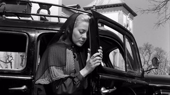 Movie still from “Viridiana” (1961), directed by Luis Buñuel – A woman looking at her cell phone while sitting in a car; Medium shot, Low angle