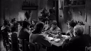 Movie still from “Viridiana” (1961), directed by Luis Buñuel – A group of people sitting around a table eating food; Wide shot, High angle