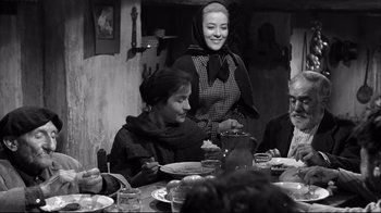 Movie still from “Viridiana” (1961), directed by Luis Buñuel – A woman standing at a table with a group of people; Medium shot, Over the shoulder angle