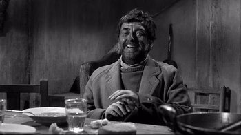 Movie still from “Viridiana” (1961), directed by Luis Buñuel – A man sitting at a table with a glass of water; Medium shot, Low angle