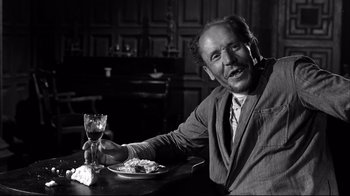 Movie still from “Viridiana” (1961), directed by Luis Buñuel – A man sitting at a table with a glass of wine; Medium shot, Low angle