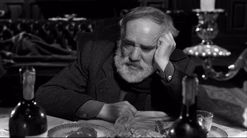 Movie still from “Viridiana” (1961), directed by Luis Buñuel – An older man sitting at a table with a glass of wine in front of him; Close Up shot, High angle