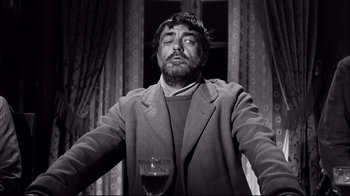 Movie still from “Viridiana” (1961), directed by Luis Buñuel – A black and white photo of a man holding a glass of wine; Medium shot, Low angle
