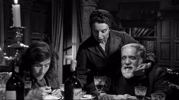 Movie still from “Viridiana” (1961), directed by Luis Buñuel – An older man sitting at a dinner table with a woman and an older man; Medium shot, Low angle