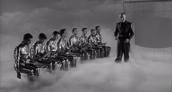 Movie still from “Visit to a Small Planet” (1960), directed by Norman Taurog – A group of men in shiny silver jackets are sitting in a row; Wide shot, Low angle