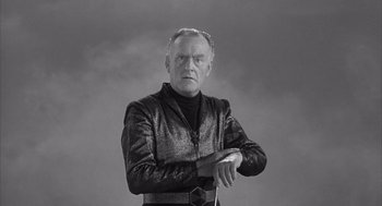 Movie still from “Visit to a Small Planet” (1960), directed by Norman Taurog – An older man wearing a leather jacket and standing in front of a gray background; Medium shot, Low angle
