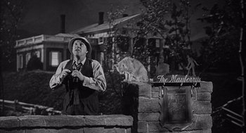 Movie still from “Visit to a Small Planet” (1960), directed by Norman Taurog – An old photo of a man and a cat sitting on a brick wall; Medium shot, Low angle