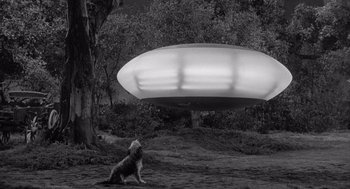 Movie still from “Visit to a Small Planet” (1960), directed by Norman Taurog – A black and white photo of a dog sitting in front of a flying saucer; Extreme Wide shot, Low angle