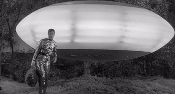 Movie still from “Visit to a Small Planet” (1960), directed by Norman Taurog – A black and white photo of a man standing in front of an object; Wide shot, Low angle