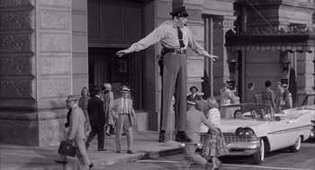 Movie still from “Visit to a Small Planet” (1960), directed by Norman Taurog – A man in a police uniform standing on the sidewalk; Wide shot, Low angle