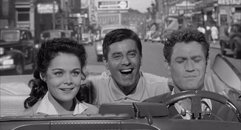 Movie still from “Visit to a Small Planet” (1960), directed by Norman Taurog – A black - and - white photo of a man and two women in a car; Medium shot, High angle
