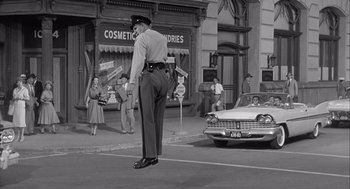 Movie still from “Visit to a Small Planet” (1960), directed by Norman Taurog – A police officer standing on the side of the road; Wide shot, Low angle