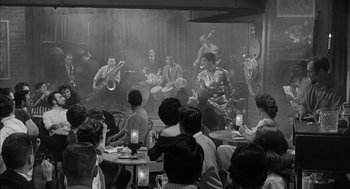 Movie still from “Visit to a Small Planet” (1960), directed by Norman Taurog – A group of people sitting at a table with musical instruments; Wide shot, High angle