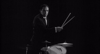 Movie still from “Visit to a Small Planet” (1960), directed by Norman Taurog – A black and white photo of a man in a suit playing drums; Medium shot, Low angle