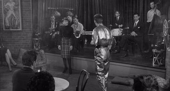 Movie still from “Visit to a Small Planet” (1960), directed by Norman Taurog – A group of men and women on a stage with instruments; Medium shot, Over the shoulder angle