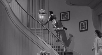 Movie still from “Visit to a Small Planet” (1960), directed by Norman Taurog – A man in a silver suit jumping a railing on a staircase; Wide shot, High angle