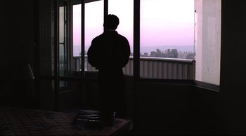 Movie still from “Vive L'Amour” (1994), directed by Tsai Ming-liang – A man standing in front of a window looking out at a city; Wide shot, Low angle