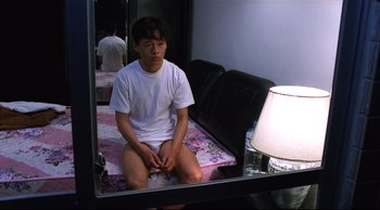 Movie still from “Vive L'Amour” (1994), directed by Tsai Ming-liang – A man sitting on a bed in front of a mirror; Medium shot, High angle