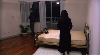 Movie still from “Vive L'Amour” (1994), directed by Tsai Ming-liang – A woman standing in front of a bed in a room; Wide shot, High angle