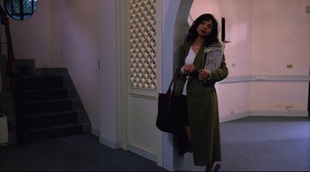 Movie still from “Vive L'Amour” (1994), directed by Tsai Ming-liang – A woman is standing in a hallway holding a newspaper; Wide shot, Low angle