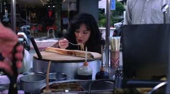 Movie still from “Vive L'Amour” (1994), directed by Tsai Ming-liang – A woman sitting at an outdoor table eating food; Medium shot, High angle