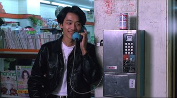 A man talking on a pay phone while wearing a leather jacket