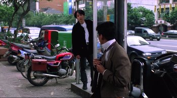 Movie still from “Vive L'Amour” (1994), directed by Tsai Ming-liang – Two men standing next to each other on the sidewalk; Wide shot, Over the shoulder angle