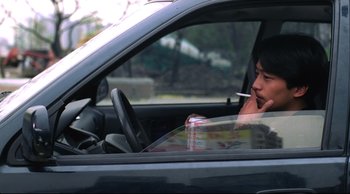 Movie still from “Vive L'Amour” (1994), directed by Tsai Ming-liang – A man sitting in the drivers seat of a car while smoking a cigarette; Medium shot, Over the shoulder angle