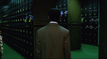 Movie still from “Vive L'Amour” (1994), directed by Tsai Ming-liang – A man wearing a suit and tie standing in front of a row of cabinets; Medium shot, Low angle