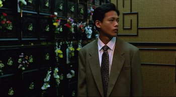 Movie still from “Vive L'Amour” (1994), directed by Tsai Ming-liang – A man in a suit and tie standing in front of flowers; Medium shot, Low angle