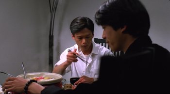 Movie still from “Vive L'Amour” (1994), directed by Tsai Ming-liang – Two men sitting at a dinner table eating food; Medium shot, Over the shoulder angle