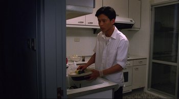 Movie still from “Vive L'Amour” (1994), directed by Tsai Ming-liang – A man in a white shirt is holding a plate in a kitchen; Medium shot, High angle