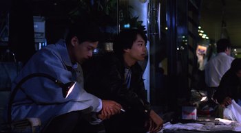 Movie still from “Vive L'Amour” (1994), directed by Tsai Ming-liang – Two young men sitting on a bench at night playing a video game; Medium shot, High angle
