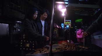 Movie still from “Vive L'Amour” (1994), directed by Tsai Ming-liang – A man and a woman standing in front of food; Medium shot, High angle