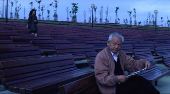 Movie still from “Vive L'Amour” (1994), directed by Tsai Ming-liang – An older man standing in front of a row of wooden benches; Medium shot, High angle