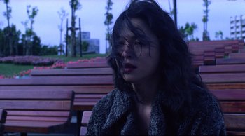 Movie still from “Vive L'Amour” (1994), directed by Tsai Ming-liang – A woman sitting on top of a wooden park bench; Close Up shot, Low angle