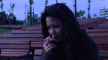 Movie still from “Vive L'Amour” (1994), directed by Tsai Ming-liang – A woman smoking a cigarette while sitting on a park bench; Close Up shot, High angle
