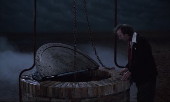 Movie still from “Voice of the Moon” (1990), directed by Richard Stanley – A man standing next to a large metal object; Wide shot, High angle