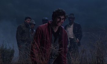 Movie still from “Voice of the Moon” (1990), directed by Richard Stanley – A group of men standing in a field at night; Medium shot, Over the shoulder angle